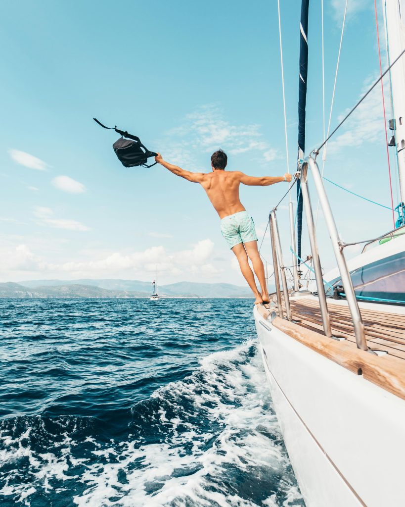 Un homme à bord d'un bateau vagué sur la mer bleuâtre, il a le bras levé vers le ciel bleu clair en signe de liberté et d'évanouissement.