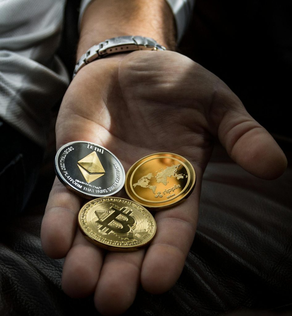Une photo d'une paume de main gauche tendue sur laquelle on peut apercevoir trois principale cryptomonnaies : Bitcoin, Ethereum, Ripple.