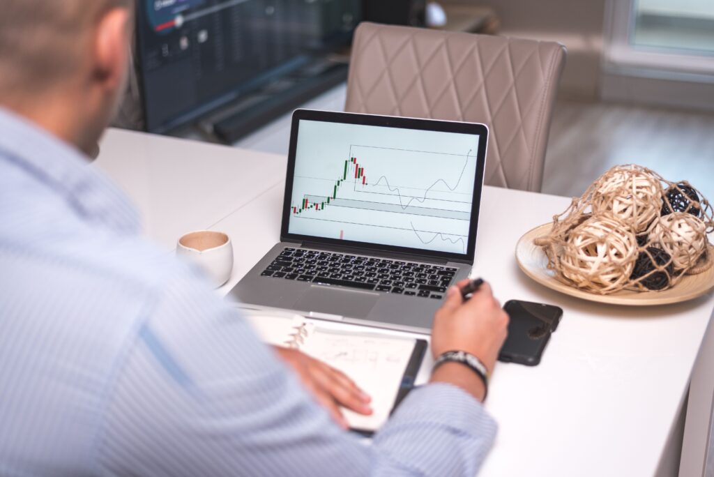 Une photo de dos d'un homme devant son ordinateur portable observant les une graphique de bourse.